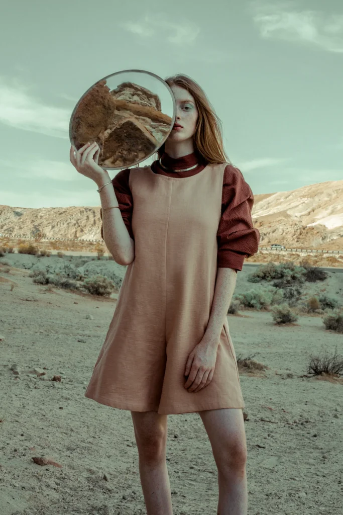 Desert editorial portrait with windswept hair, pale neutral clothing and a sculptural headpiece.