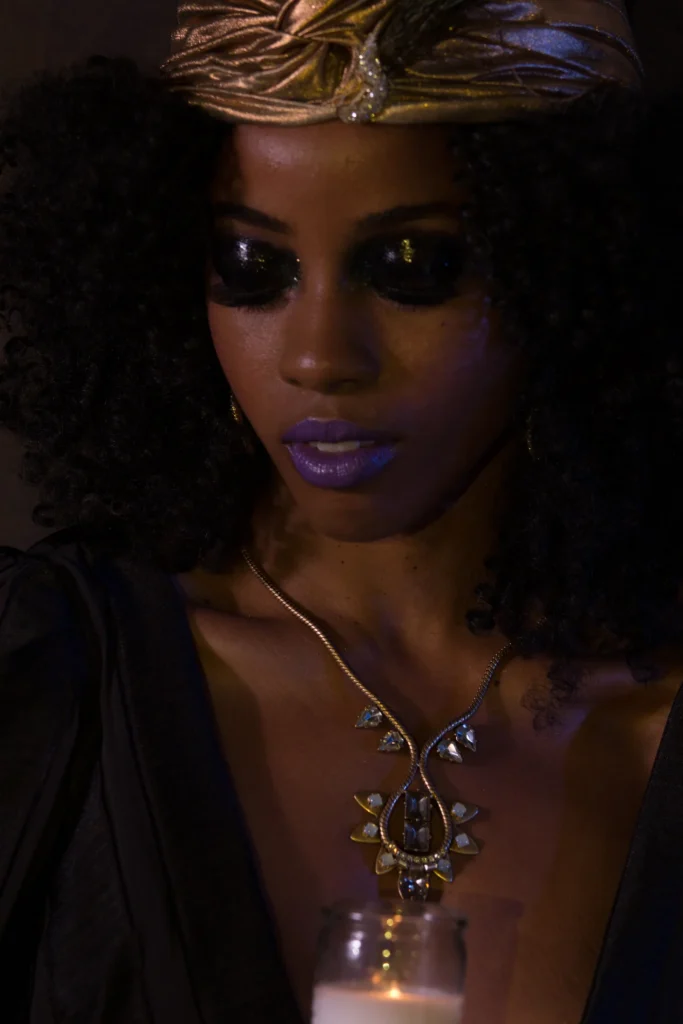 Beauty portrait with purple lips, dramatic eye makeup and a sculptural headwrap.