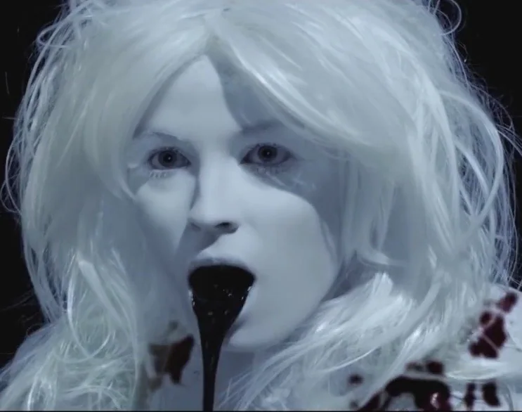 Character portrait with a short white wig, pale complexion and dark lips.