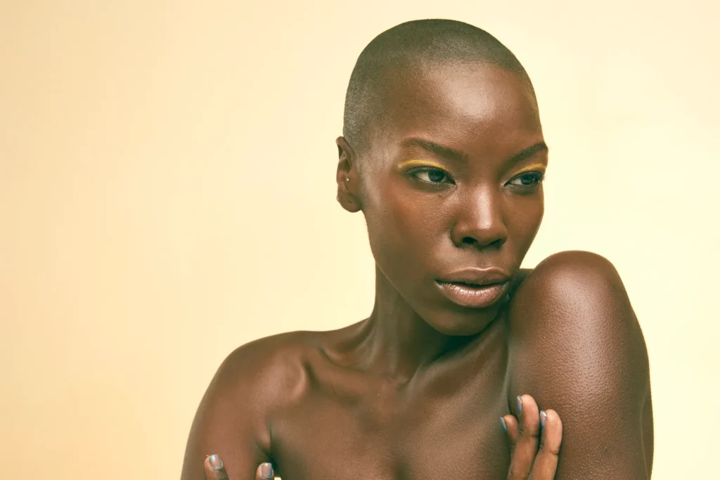 Studio beauty portrait with closely cropped hair, green eye makeup and gold-toned skin.