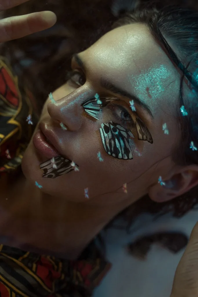 Close-up editorial portrait with metallic green makeup and butterflies around the face.