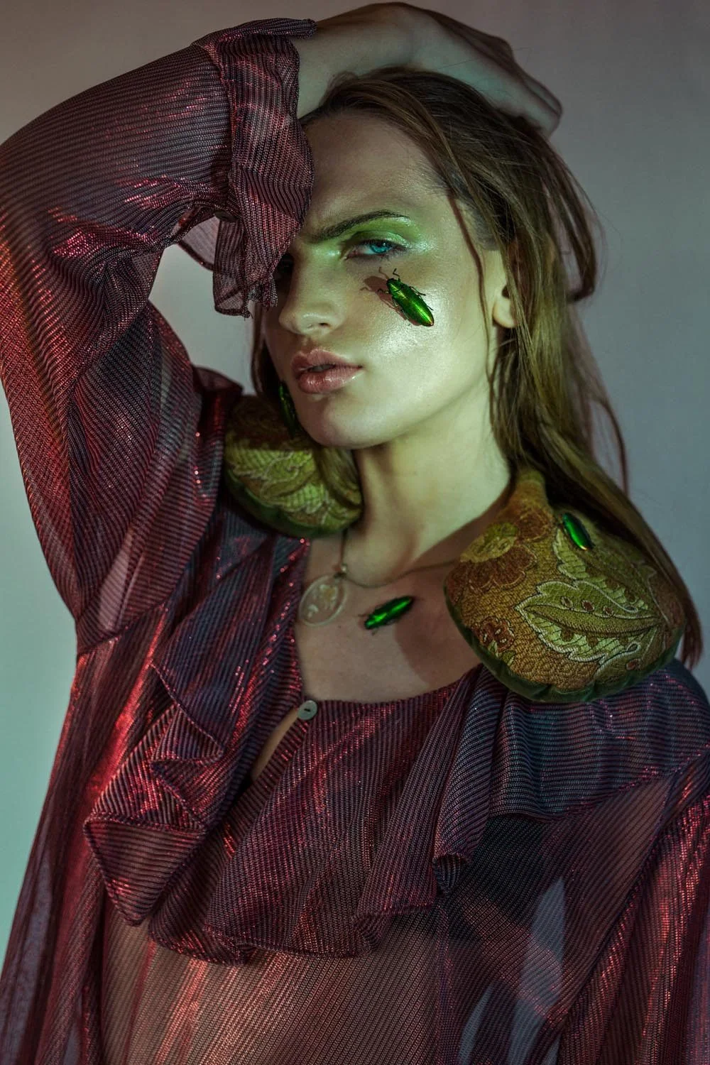 Editorial portrait with shimmering green eye makeup, muted lips and butterflies on the face and shoulder.